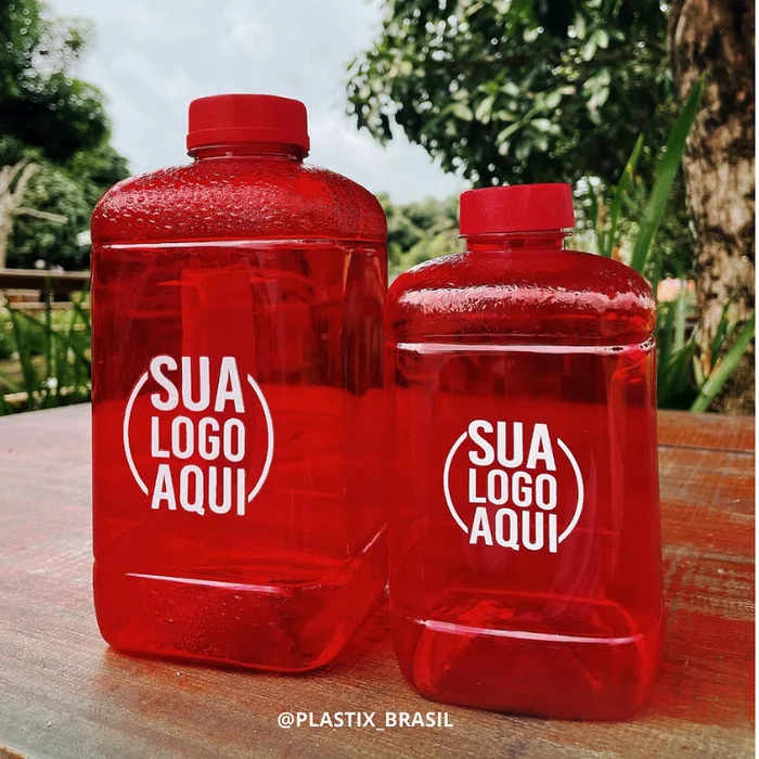 Dois Galões Fit vermelhos com a arte "Sua logo aqui" sobre uma mesa ao ar livre
